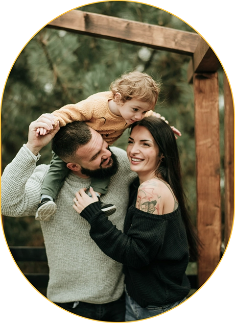 Family hugging while smiling with child on dad's shoulders.